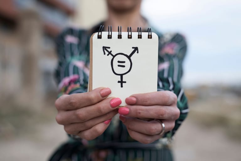 Transgender: Leben im falschen Körper; Frau hält Notizbuch mit Transgendersymbol in die Kamera