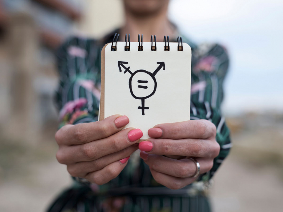 Transgender: Leben im falschen Körper; Frau hält Notizbuch mit Transgendersymbol in die Kamera